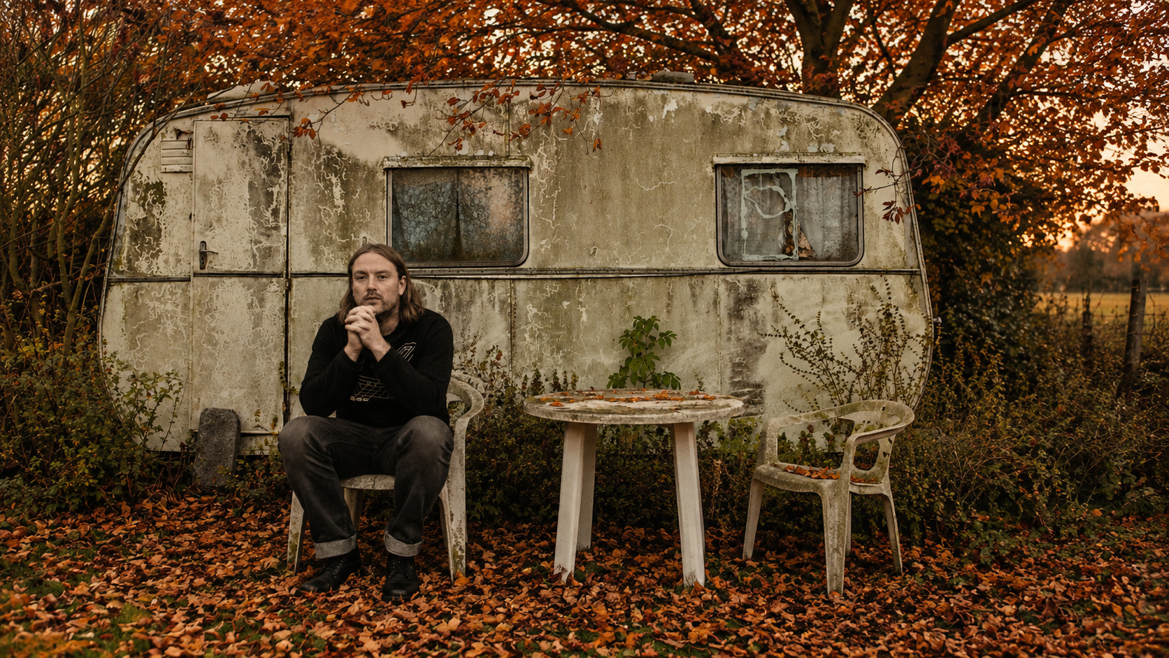 Dan Carney assis devant une vieille caravane sous des arbres d’automne.